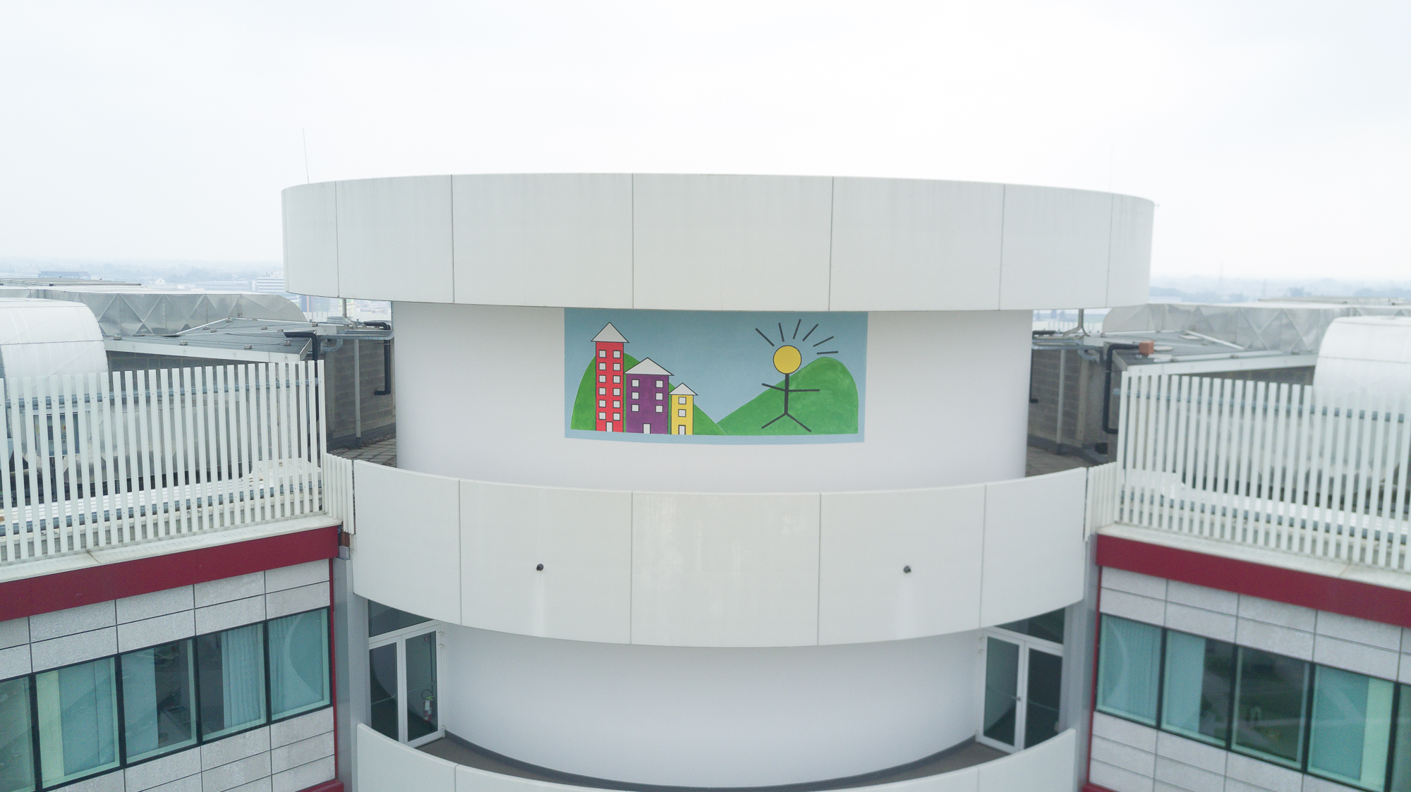 Si vede l'ultimo piano della torre di Città della speranza con il disegno colorato di tre edifici e un uomo con la testa a forma di un sole