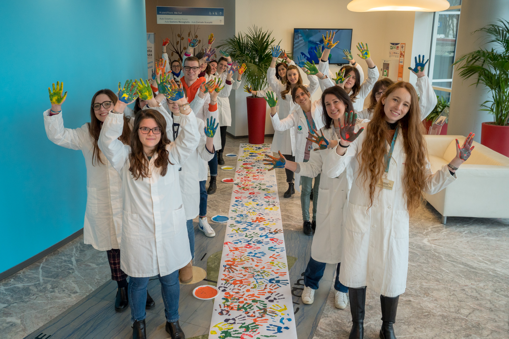 immagine con un gruppo di donne dentro l'edificio di Città della speranza con mani alzate e colorate. Per terra un telo pieno di mani colorate