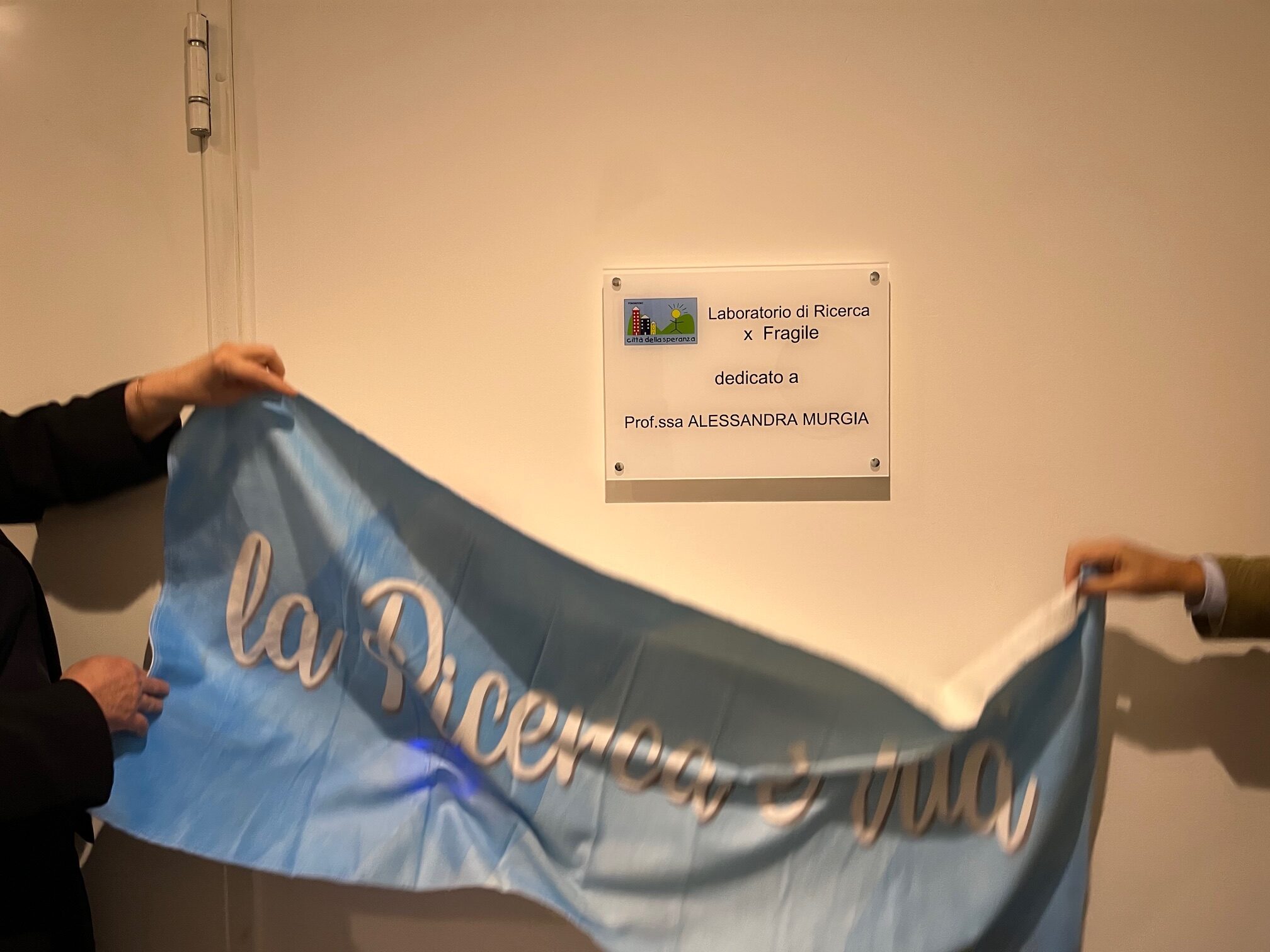 Viene tolta la bandiera che svela la targa dedicata alla prof.ssa Murgia
